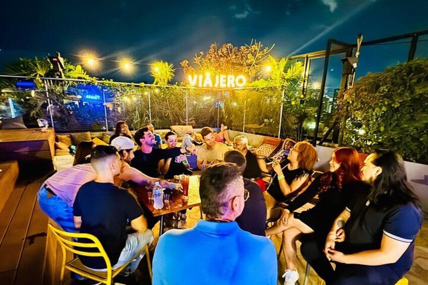A group of people sitting outdoors at night, with a sign reading 'VIAJERO' above them. 2
