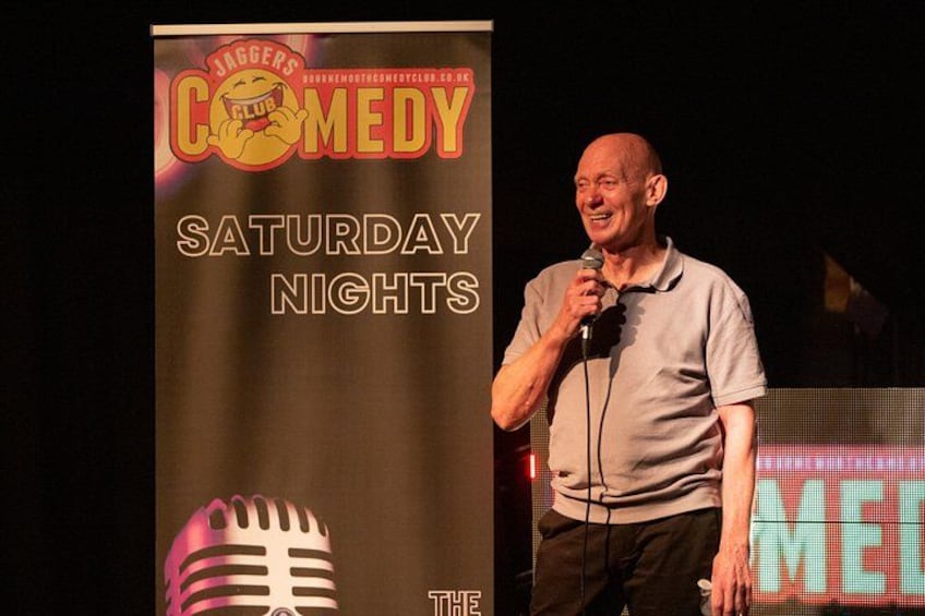 A man on stage with a microphone, a sign for 'Jagger's Comedy Saturday Nights', and a retro microphone graphic. 2