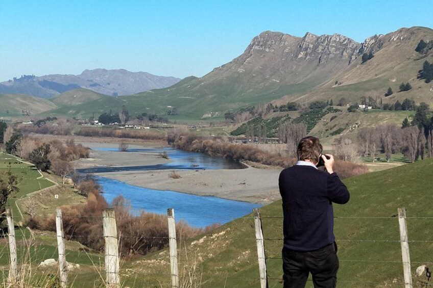Eine Person fotografiert einen Fluss mit Bergen im Hintergrund. 5