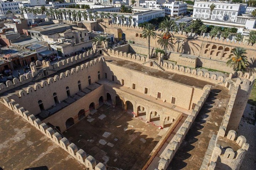 Vue aérienne d’un site historique fortifié, doté d’une vaste cour, entouré de murs et de palmiers. 3