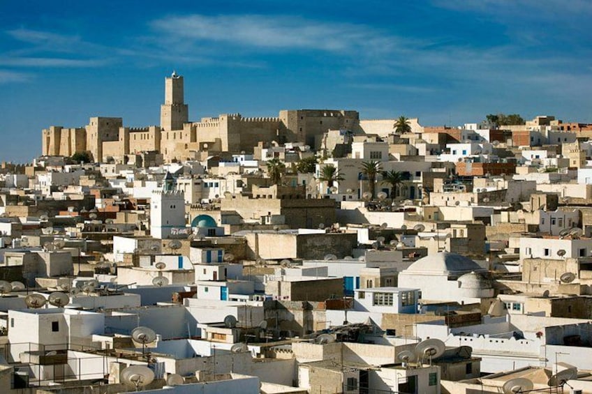 Un paysage urbain dense, caractérisé par une architecture historique, avec notamment une imposante structure fortifiée en arrière-plan. 2