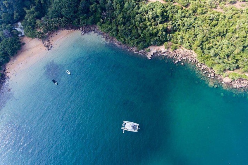 Una zona costera con playa arenosa, un barco pequeño en el agua y un bosque verde frondoso. 2