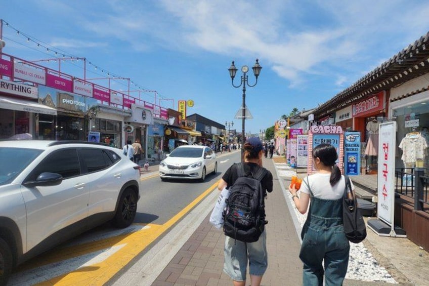 A street with shops, pedestrians, and parked cars. 5