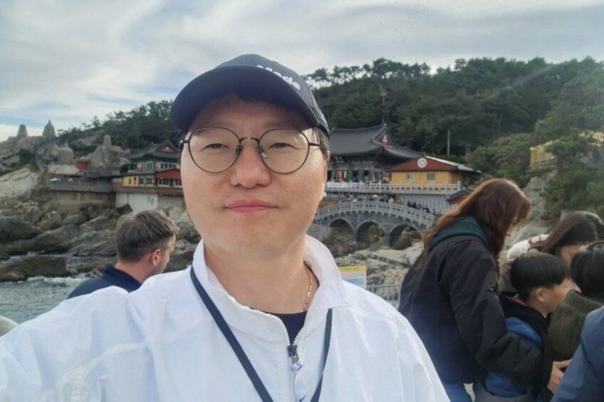 A person in a white jacket and cap, with a traditional building and rocky landscape in the background. 2