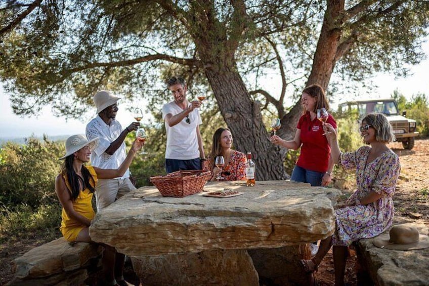 Eine Gruppe von Personen sticht Weinbecher um einen Steintisch im Freien an. 3