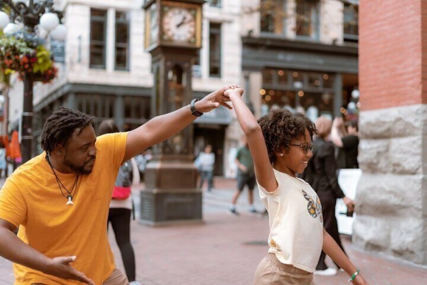 Two people dancing in a public square with a clock tower in the background. 4