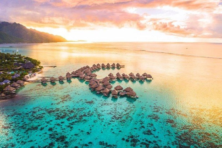 An aerial view of overwater bungalows arranged in a heart shape, surrounded by turquoise waters and a sunset sky. 3