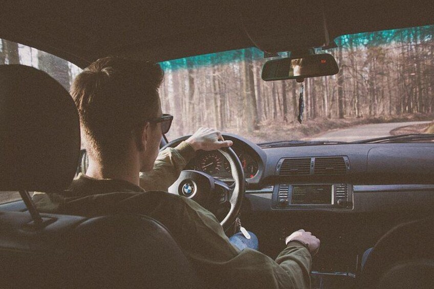A person driving a car with a steering wheel, dashboard, and rearview mirror. 3
