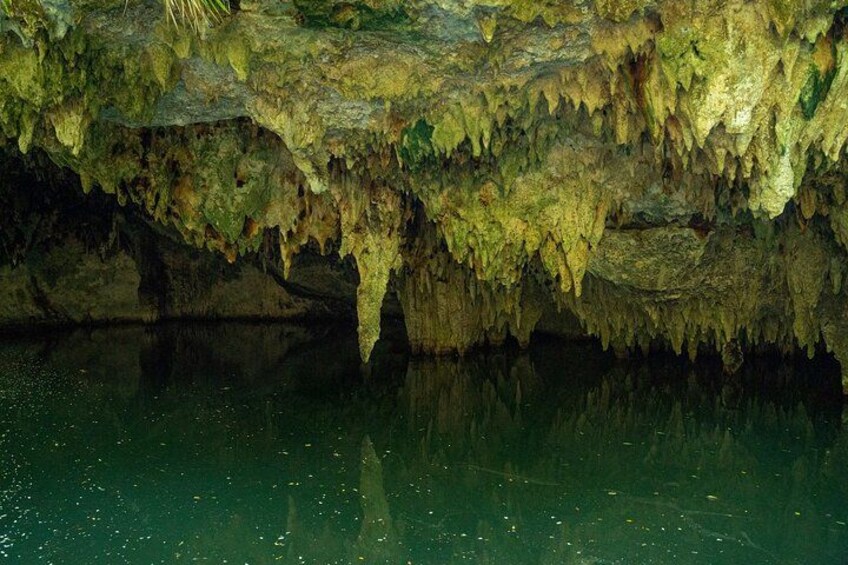 Interno di una grotta con stalattiti e stalagmiti, l'acqua riflette il soffitto e una pozza tranquilla in basso. 2