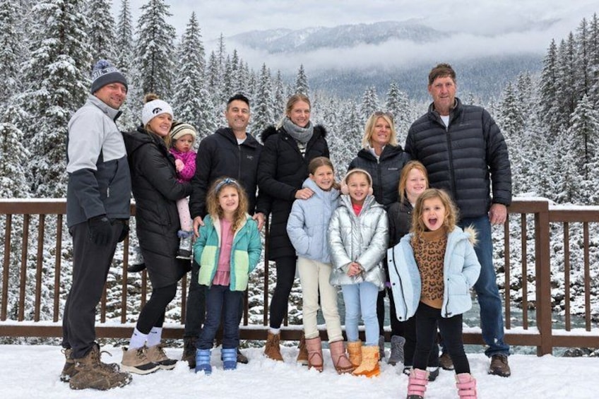 A group of people standing on a wooden deck with snow-covered trees and mountains in the background. 4