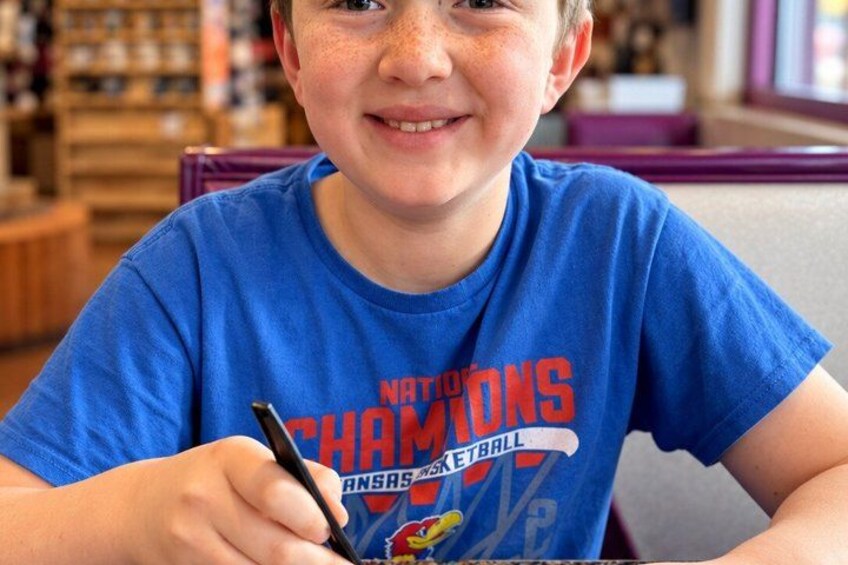 A person wearing a blue t-shirt with a sports team logo and text, sitting at a table with a pen in hand. 5