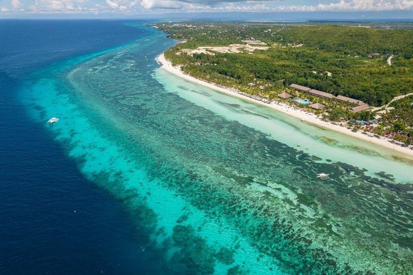 A coastal landscape with clear turquoise waters, a sandy beach, and a dense green forest. 1