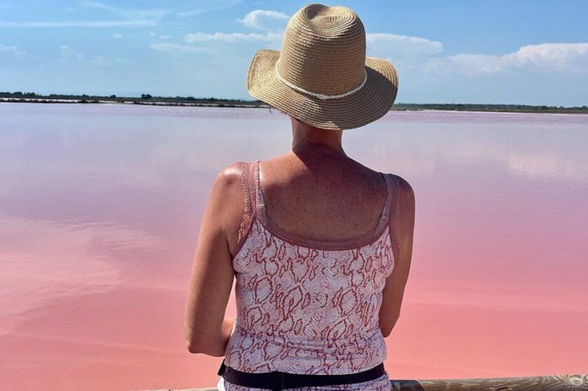 A person wearing a straw hat and a patterned tank top, standing by a pink body of water. 1