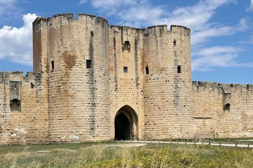 A historic stone castle with a large arched entrance, surrounded by a grassy area and a clear blue sky. 2