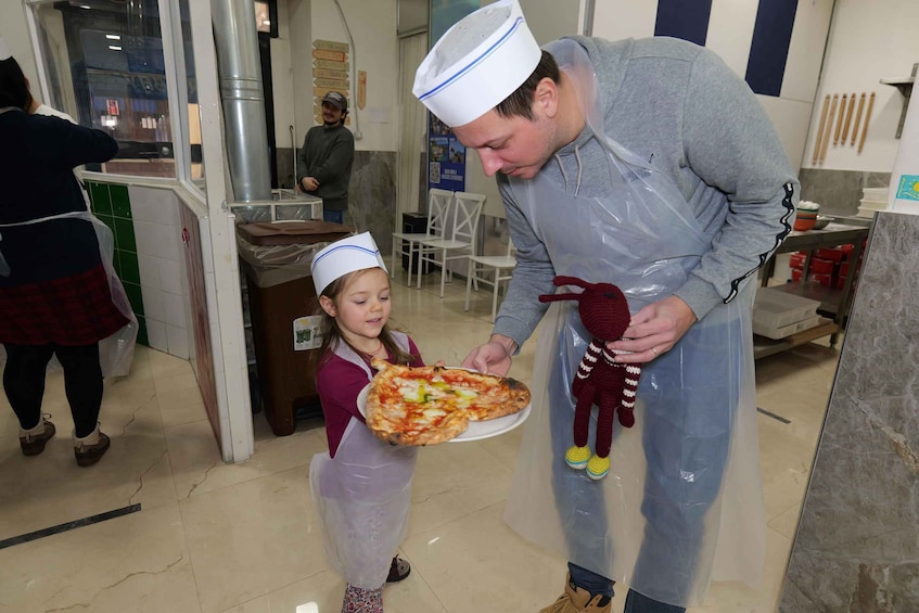 A person handing a pizza to a child in a kitchen setting. 2