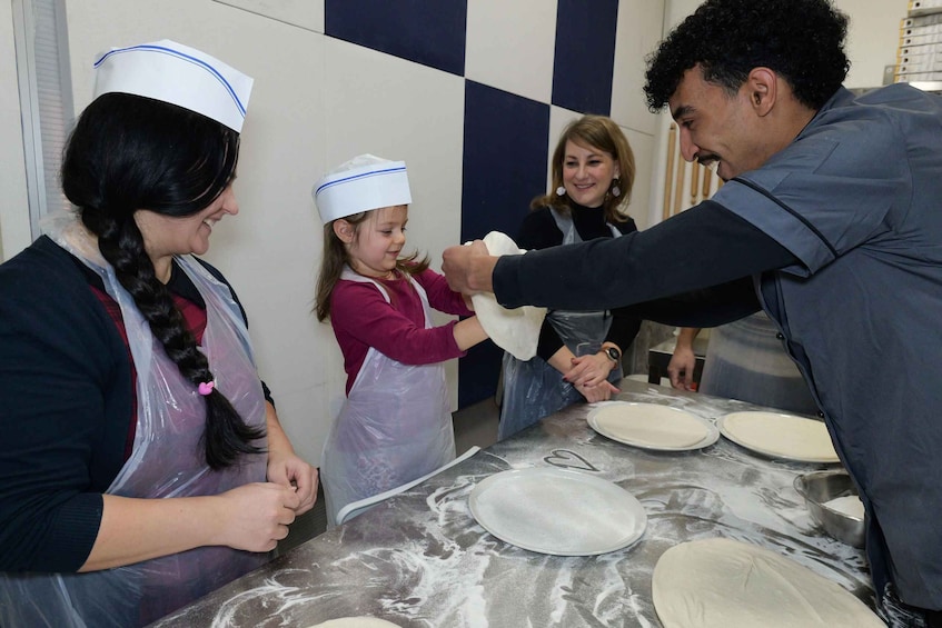 A group of people engaged in a dough preparation activity, with flour-covered surfaces and dough on plates. 4