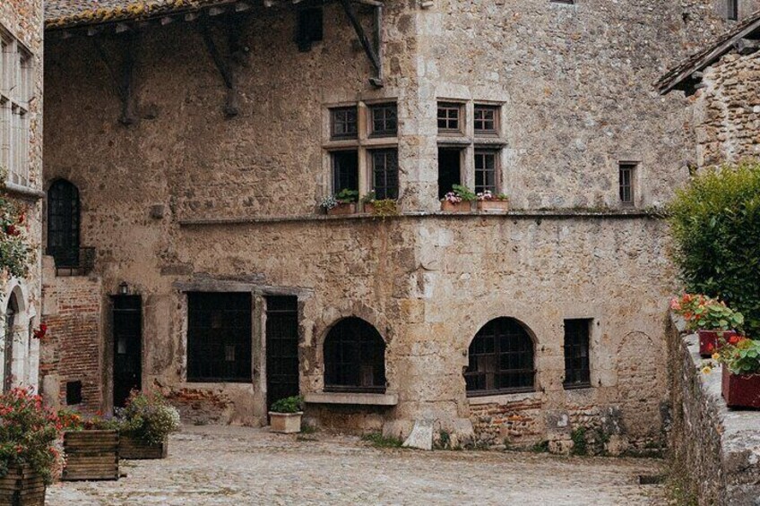 Un edificio storico in pietra con finestre ad arco e portali, un cortile in selciato e piante in vaso. 3