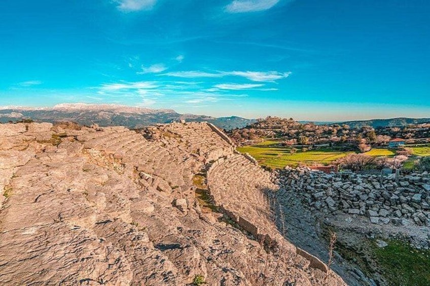 A rocky terrain with a stone wall, a valley with fields, and distant mountains under a clear sky. 1