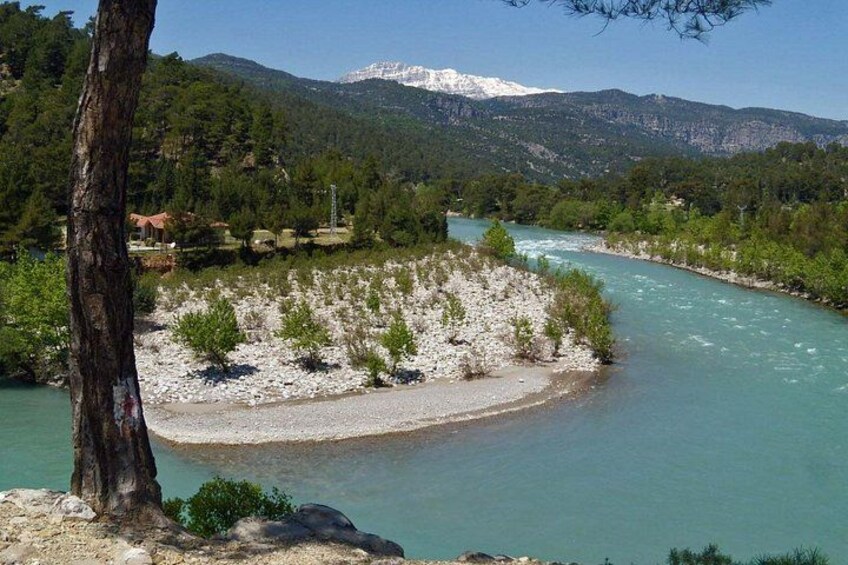 A river flowing through a rocky landscape with a tree in the foreground and mountains in the background. 2