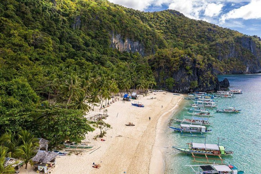 A beach with boats, palm trees, and a mountainous backdrop. 2