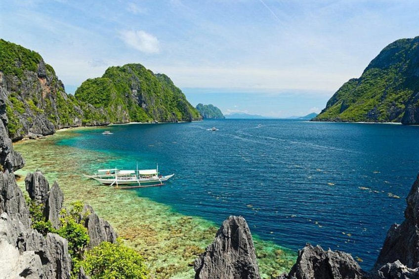A boat on a clear turquoise sea, surrounded by rocky cliffs and lush green hills. 4