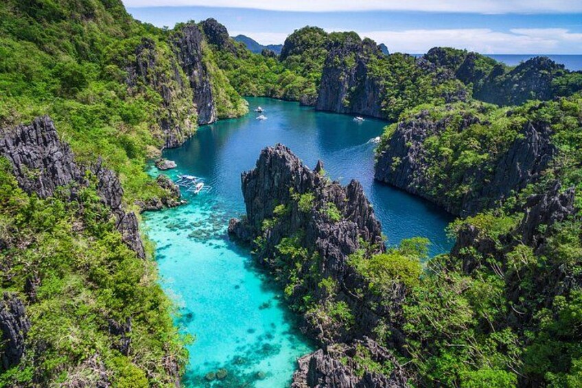 A coastal landscape with clear turquoise waters, rocky cliffs, and dense green vegetation. 1