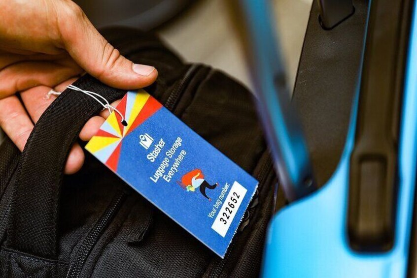 A hand holding a luggage tag with a blue background and a red and yellow design. 1