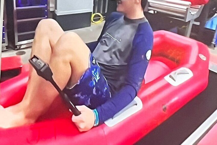 A person in a blue and black wetsuit sitting on a red inflatable raft. 4