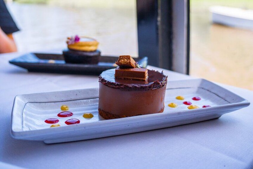 A dessert on a white plate with a chocolate base and a caramel topping, accompanied by colorful edible flowers. 2