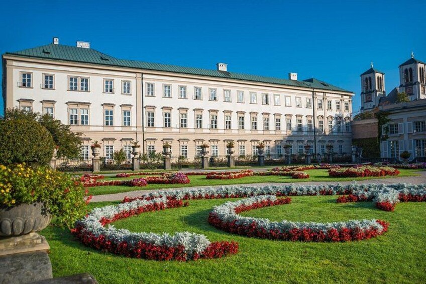 A large building with a green roof and a garden with red and white flowers. 4