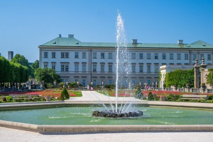 Ein großes Gebäude mit einem begrünten Dach, einer Fontäne und einem gepflegten Garten. 2