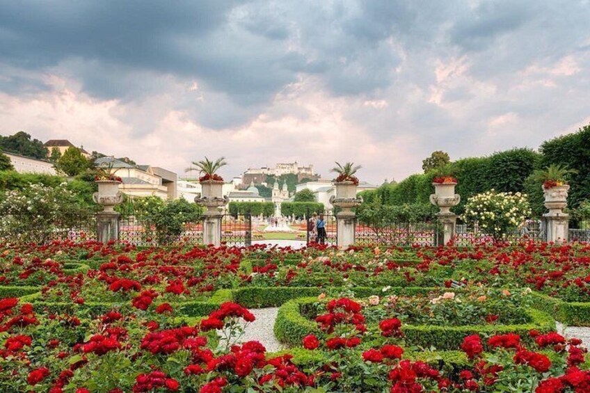 A garden with red flowers, a fountain, and a statue. 2