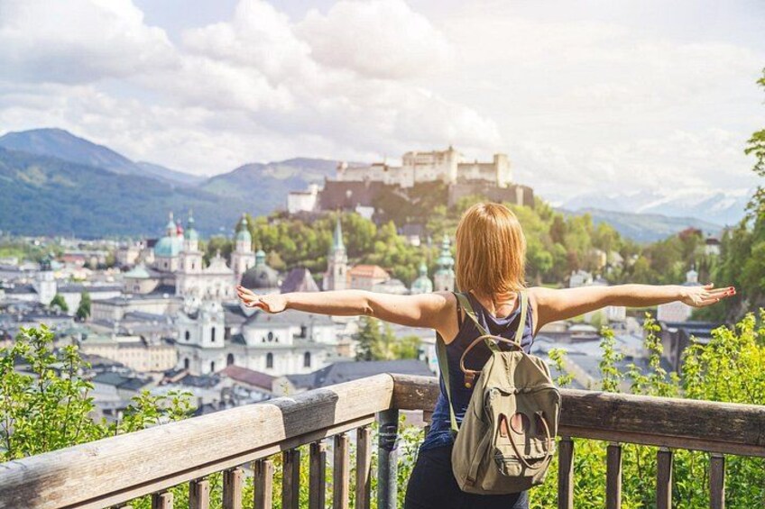 A person with arms outstretched, overlooking a cityscape with historic buildings and a castle on a hill. 2