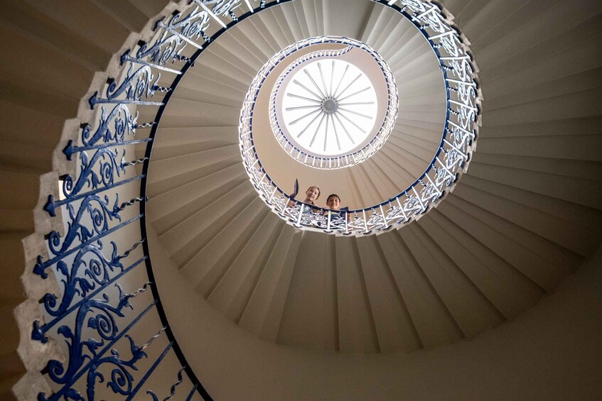 Una escalera de caracol con barandillas metálicas azules ornamentadas y un techo blanco con diseño de sol. 2