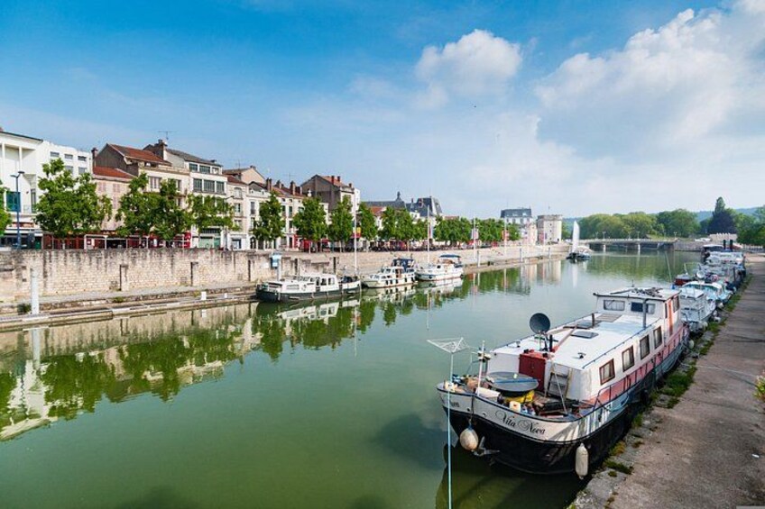 A river with boats docked along the shore, a bridge, and buildings lining the riverbank. 5