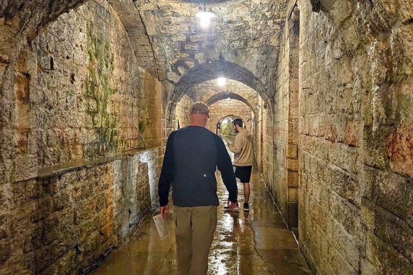 A stone tunnel with wet walls and a person walking towards the end. 3