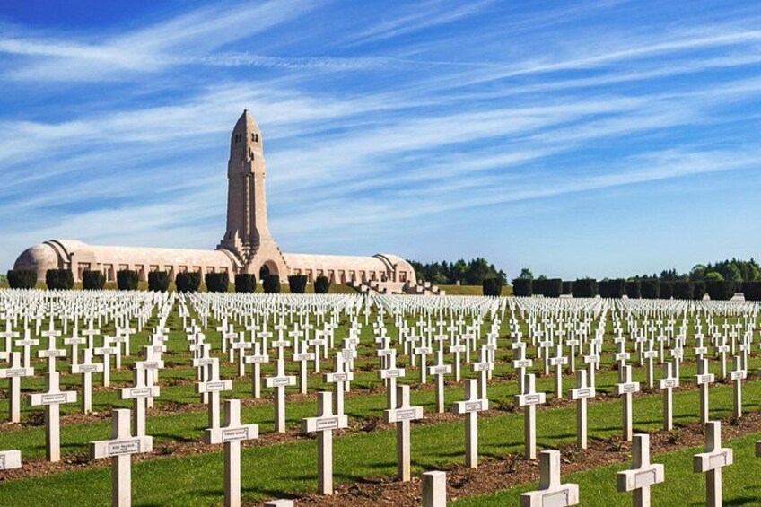 A cemetery with numerous white crosses and a large building with a tall tower in the background. 1