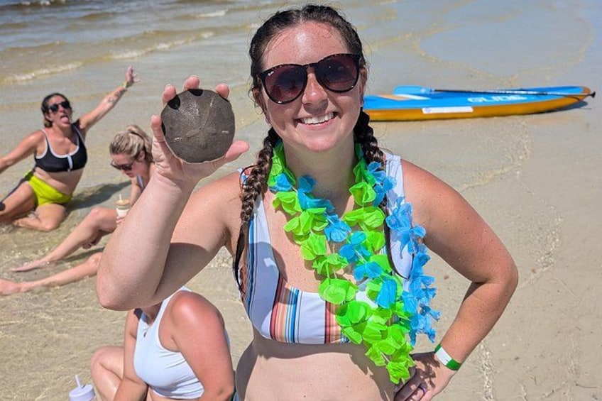 Una persona sostiene una concha marina en la playa, con otras personas al fondo. 3