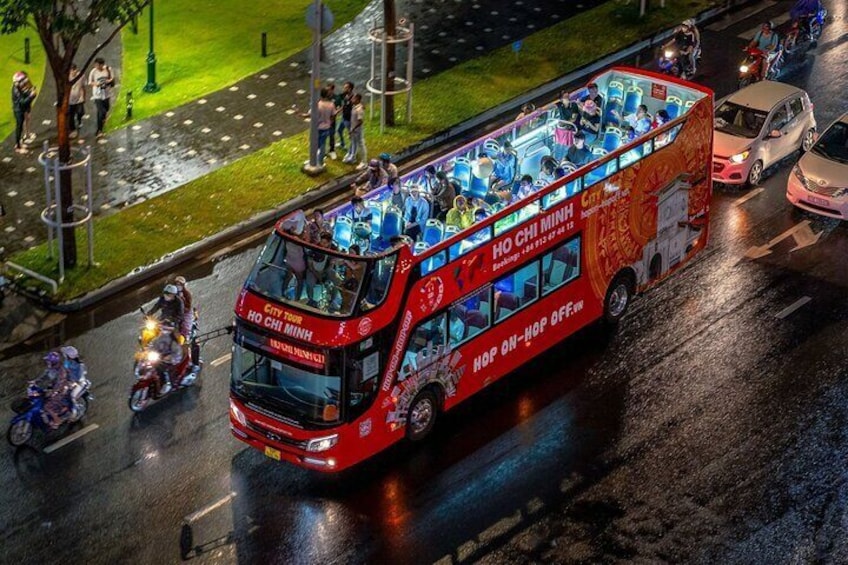 Un autobus à deux étages rouge, orné de publicités sur ses flancs, roule sur une chaussée mouillée, entouré d’autres véhicules. 2