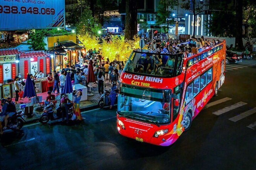 Un autobus à deux étages rouge, portant l’inscription « VISITE DE HÔ-CHI-MINH-VILLE », roule dans une rue animée, de nuit. 4