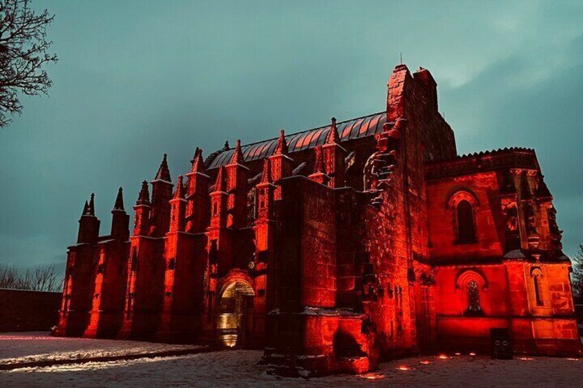 A large, historic building with multiple towers and a prominent archway, illuminated by red lighting. 1