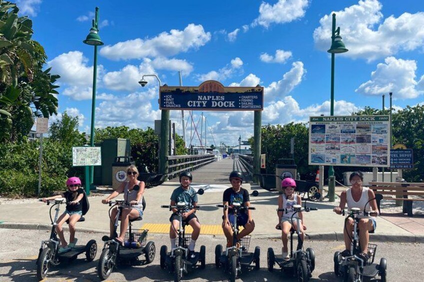 Personas montando segways en una calle con un cartel de Naples City Dock. 1
