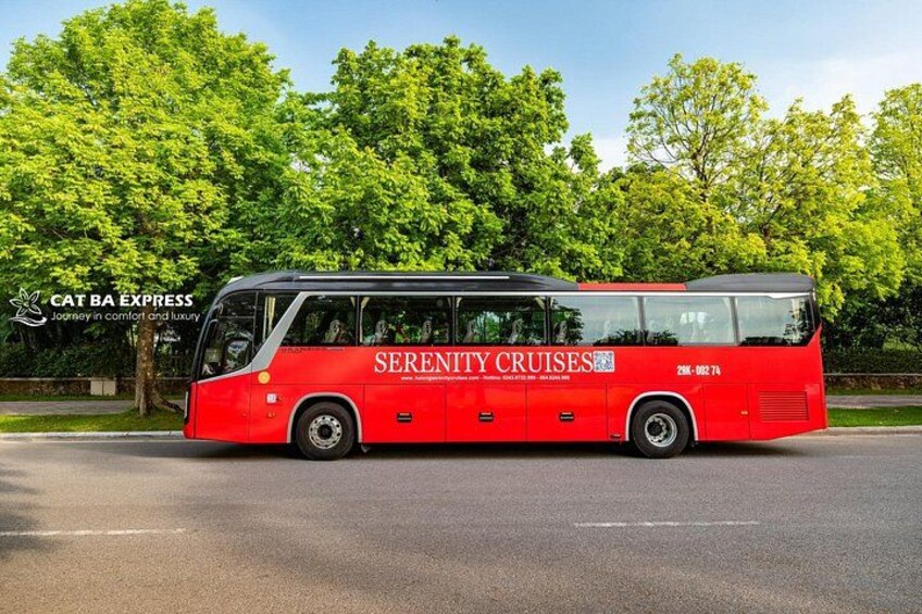 A red bus with 'Serenity Cruises' branding on the side, parked on a road with trees in the background. 1