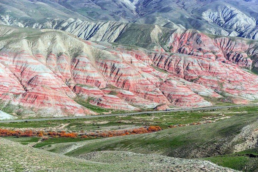 A landscape with layered rock formations in shades of pink and white, a road, and a distant view of mountains. 3