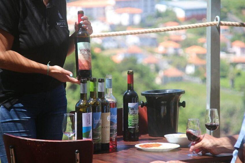 A person pouring wine from a bottle, a table with wine bottles, glasses, and a black pot. 1