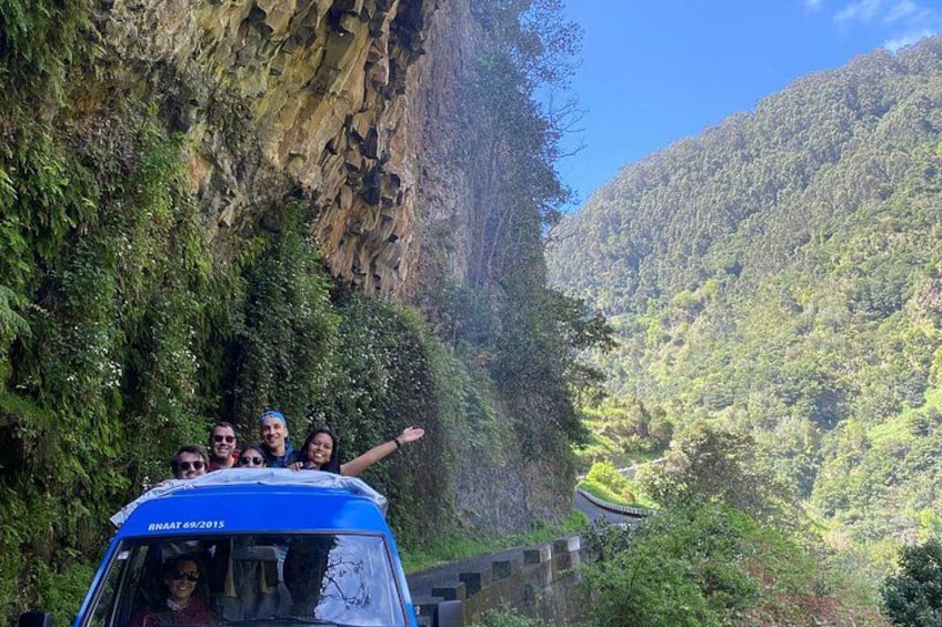 A vehicle with people on top, surrounded by steep cliffs and lush greenery. 2