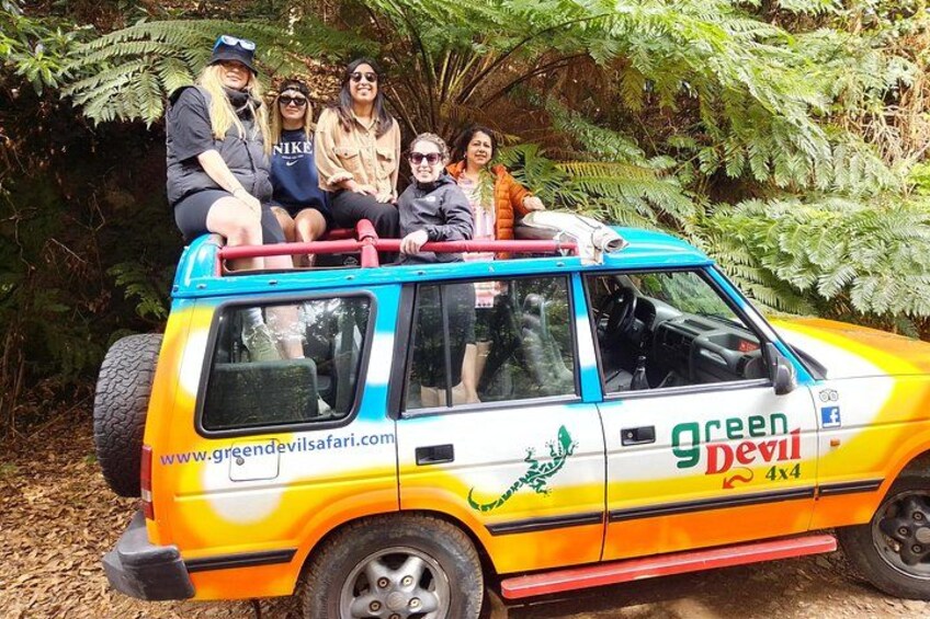 A colorful SUV with people on top, parked in a forested area. 3