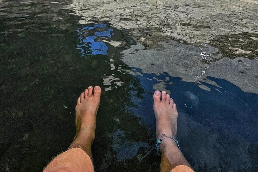 A pair of bare feet standing in clear water with a bracelet on one ankle. 4