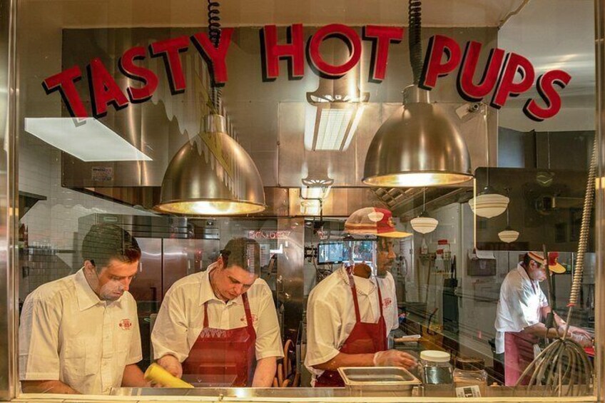 Eine Küche mit drei Köchen, die Essen zubereiten, mit einem Schild mit der Aufschrift 'TASTY HOT PUPS'. 2