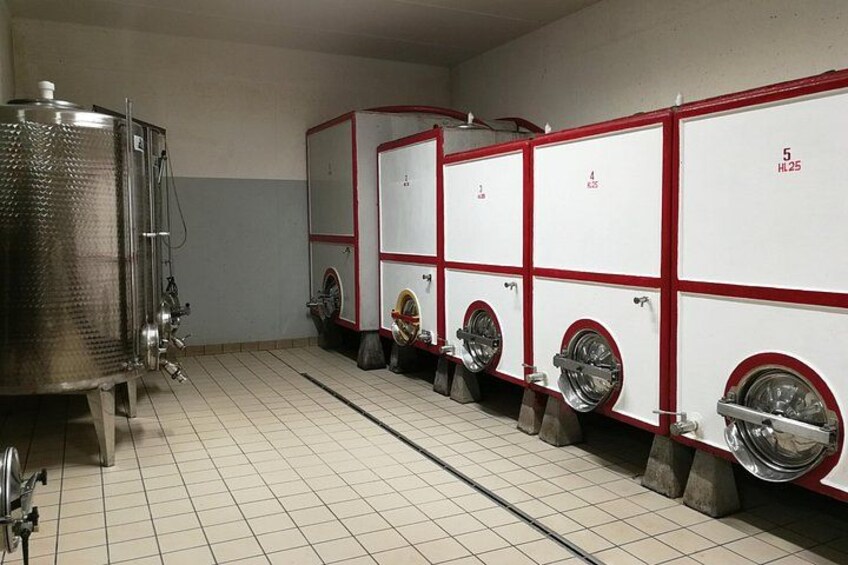 A row of industrial washing machines with red frames and wheels, a large stainless steel tank, and a tiled floor. 3